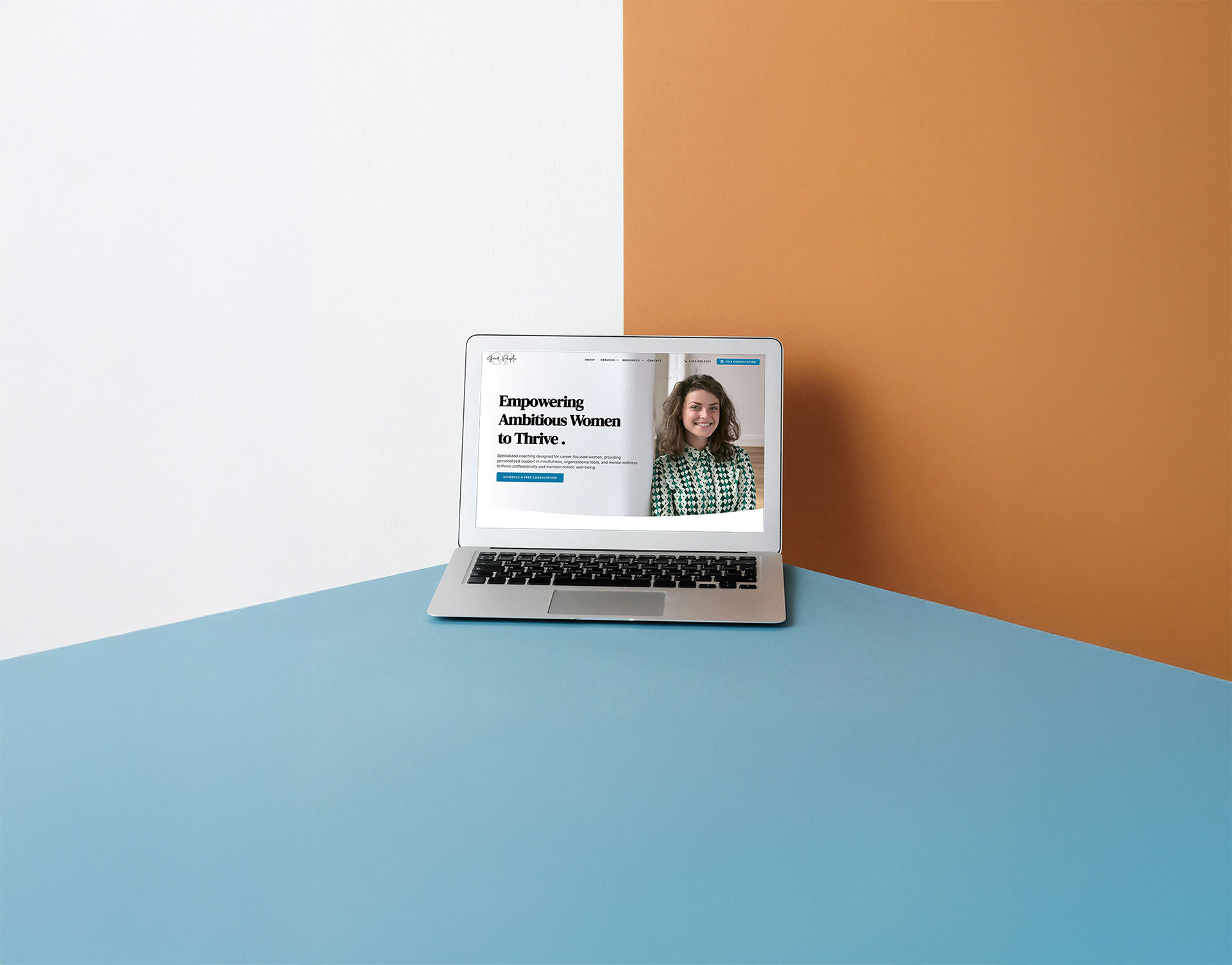 laptop with a beautifully designed website sitting on a blue surface in front of a white & burnt orange colored background