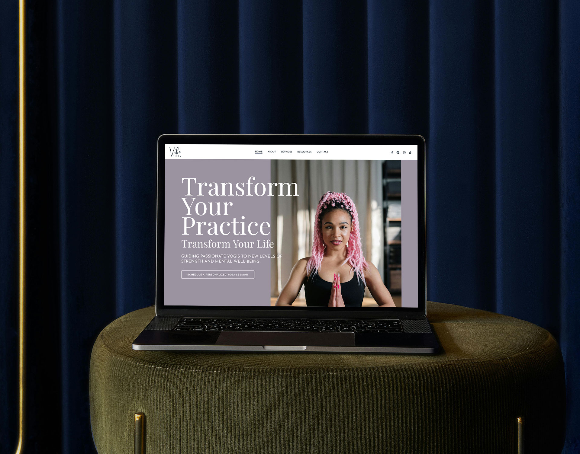 laptop with a beautifully designed website sitting on a olive green velvet ottoman in front of a dark navy blue velvet curtain